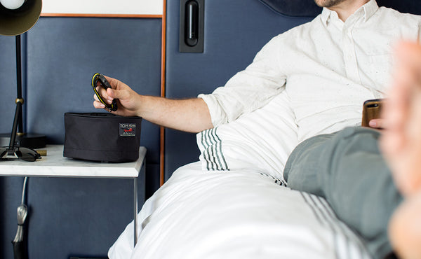 A person placing a wristwatch into a Large Travel Tray set up on a hotel side table.